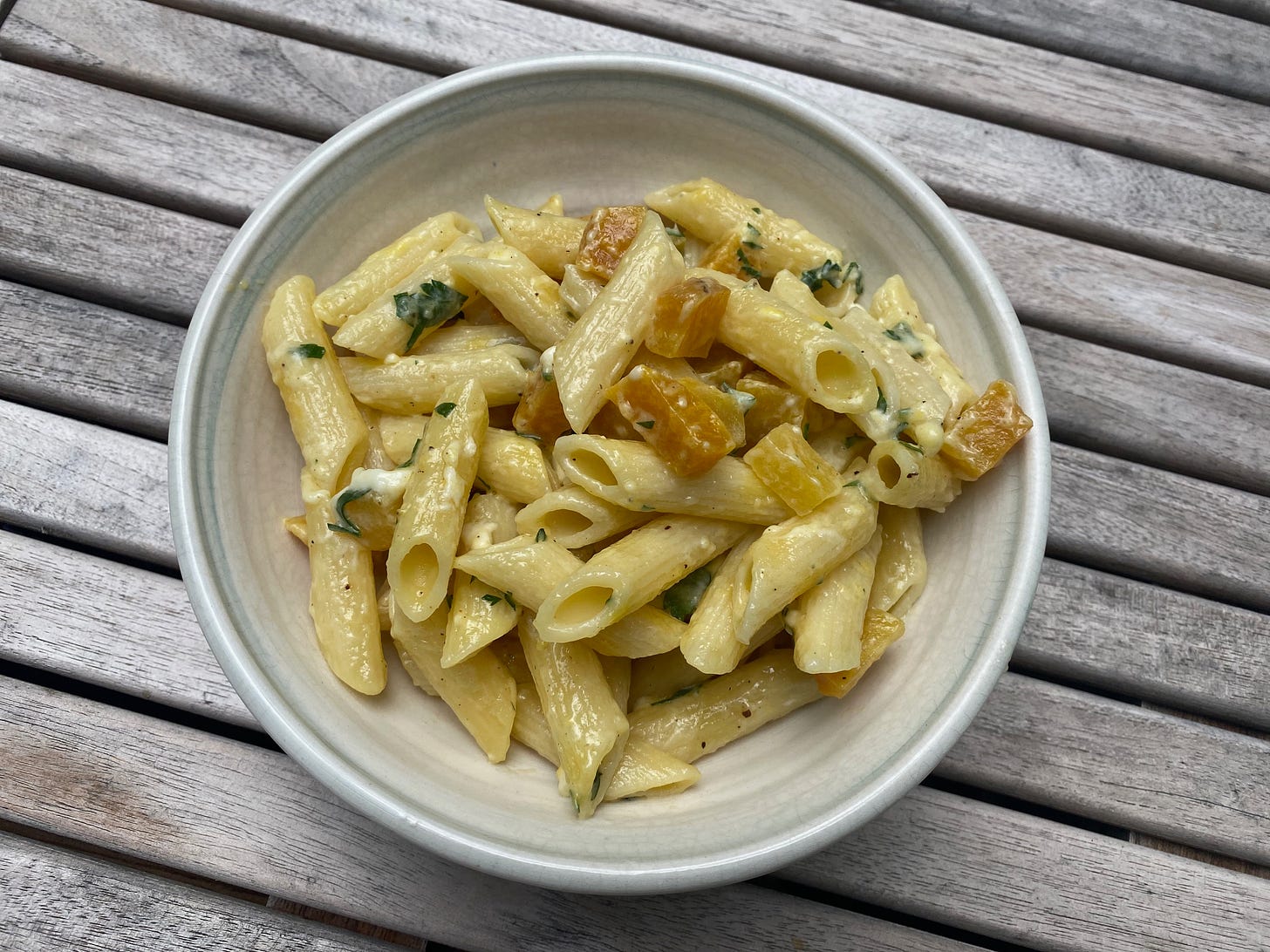 A while ceramic bowl filled with cheesy penne and cubes of roasted golden beets.