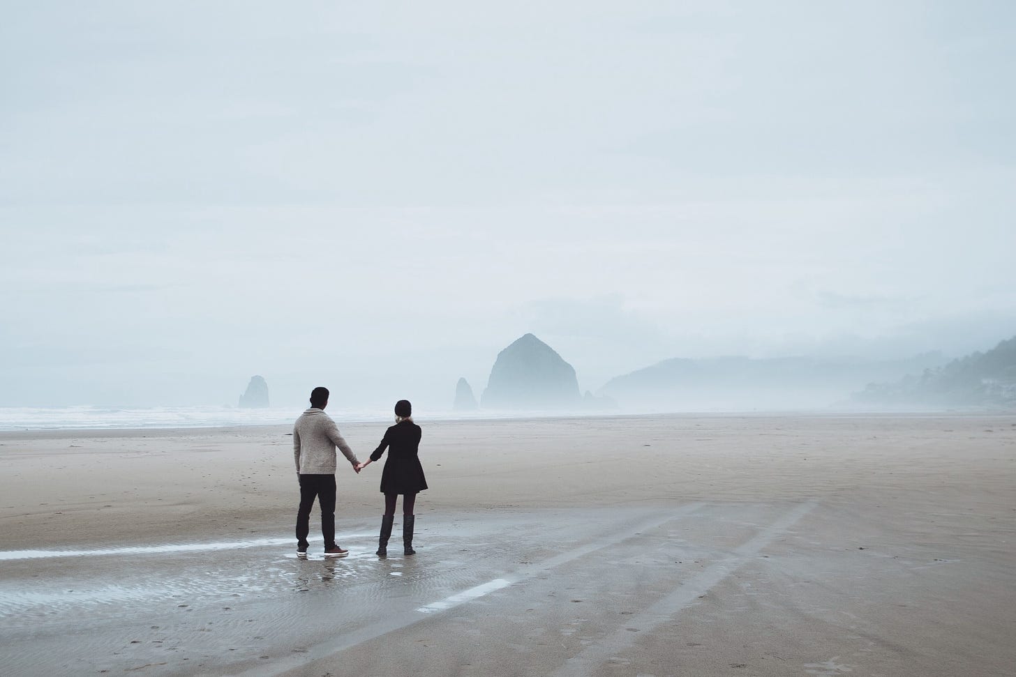 A couple walks alone on a deserted beach in heavy fog.
