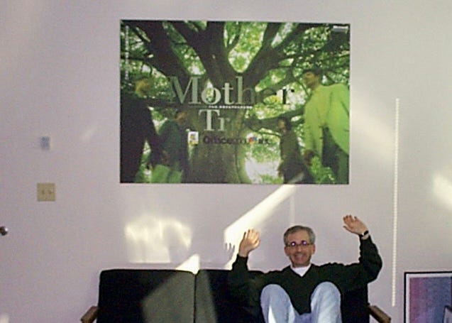 Photo of me sitting on a sofa in my office showing off the Mother Tree poster hanging on the wall.