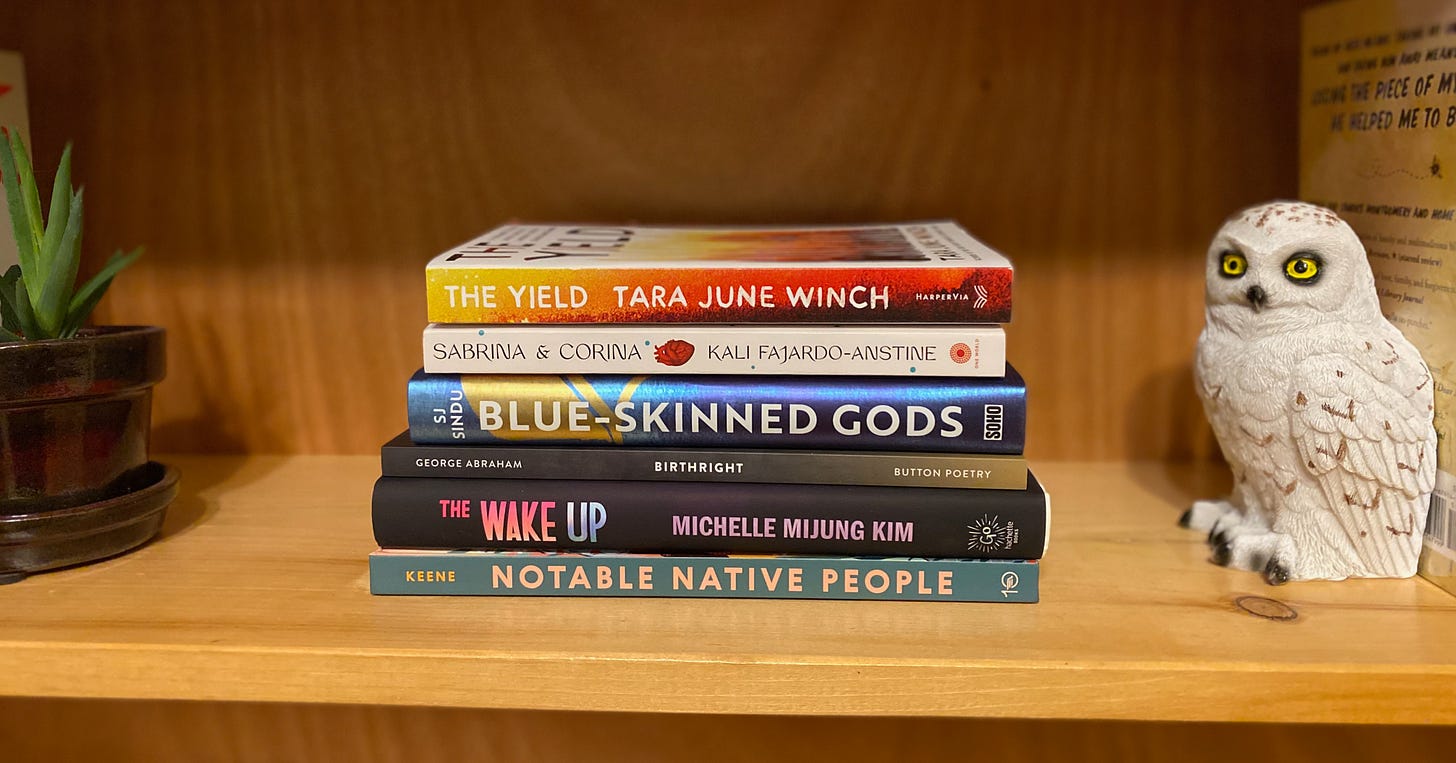 A stack of books on a wooden shelf, laying flat with their spines facing out. They sit between a succulent in small brown pot and a snowy owl bookend. Books are: Notable Native People, The Wake Up, Birthright, Blue-Skinned Gods, Sabrina & Corina, and The Yield.