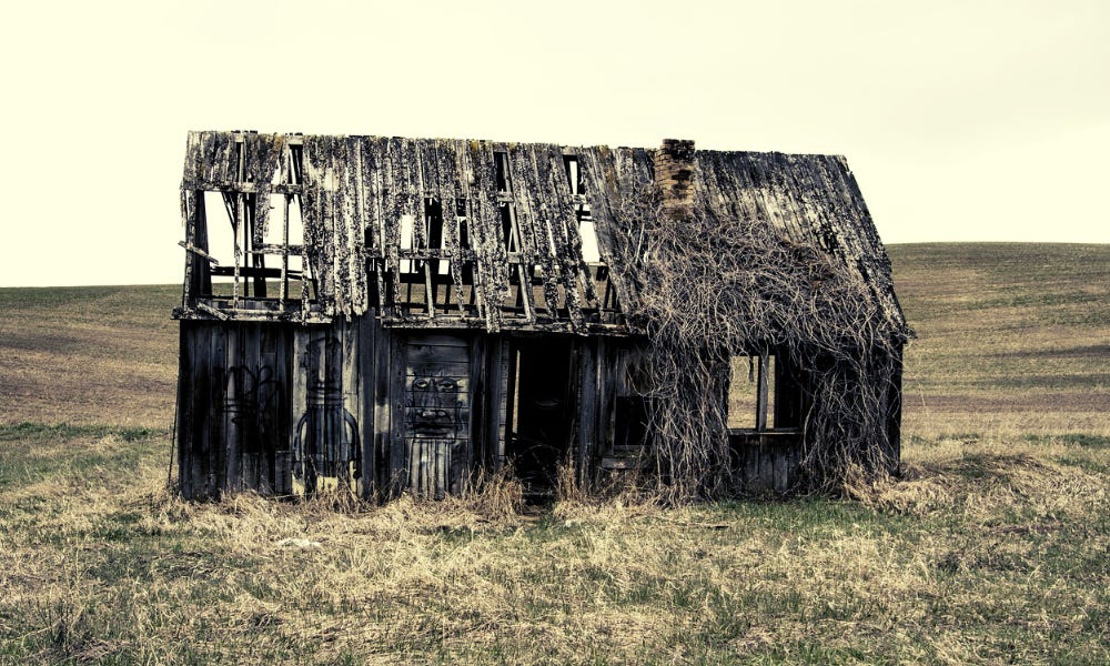 Abandoned farm house or barn in the middle of a grassy field.