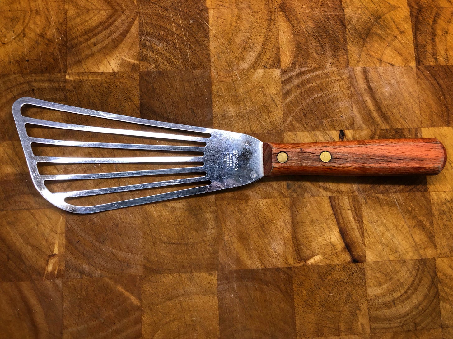 Wood-handled metal fish spatula on a cutting board