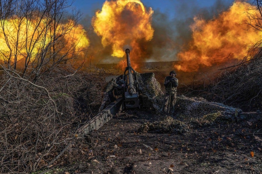Two soldiers operate a piece of artillery, which spews flames from its muzzle as they fire.