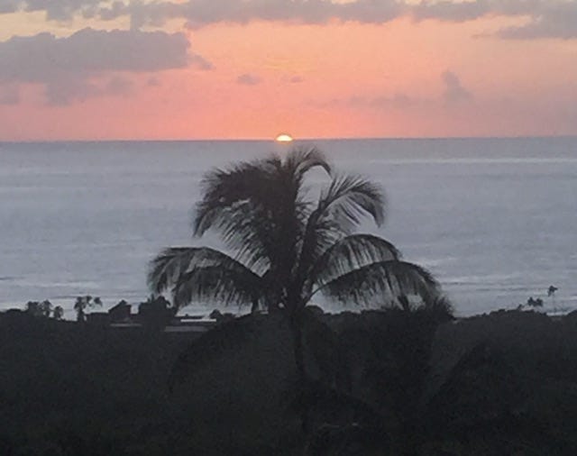 Sun barely visible as it seems to descend into the ocean during sunset in Hawaii.