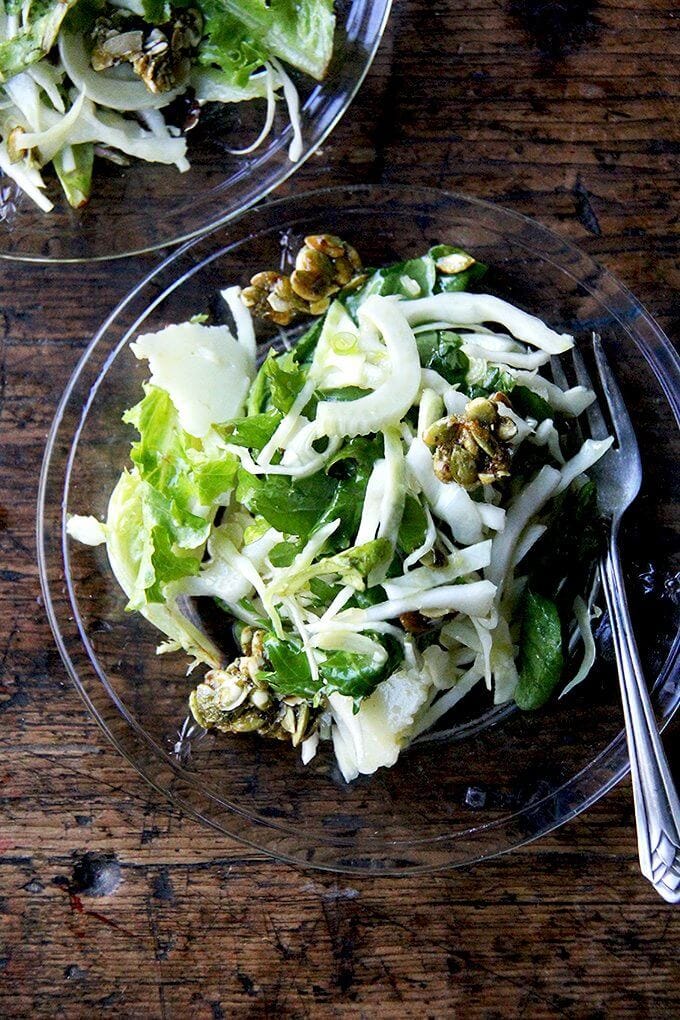 Two plates of a fall salad with cabbage, fennel, greens, and candied pepitas.