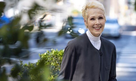 Woman wearing black suit and white turtle neck smiles as she looks into the camera