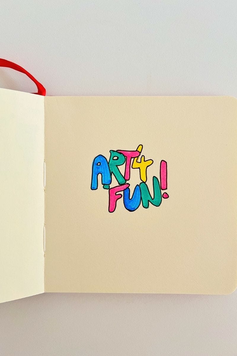 Image: a photo of a square red colour cover sketchbook with a doodle of the words Art 4 Fun. The font is a retro-looking font with black outline, coloured in with bright pink, blue, yellow and green each for the different alphabets. 