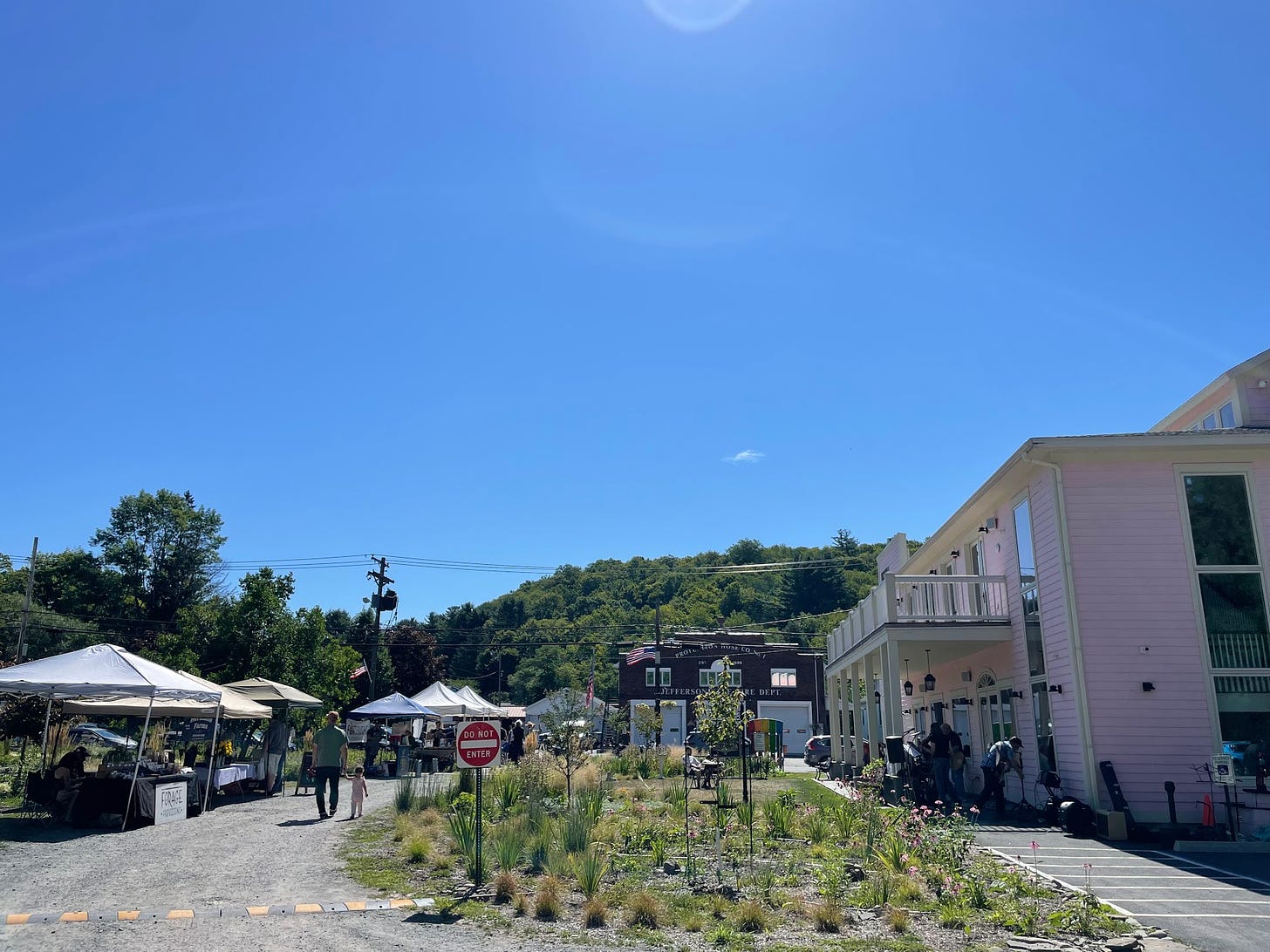 A farmer's market in a parking lot, behind which green hills can be seen