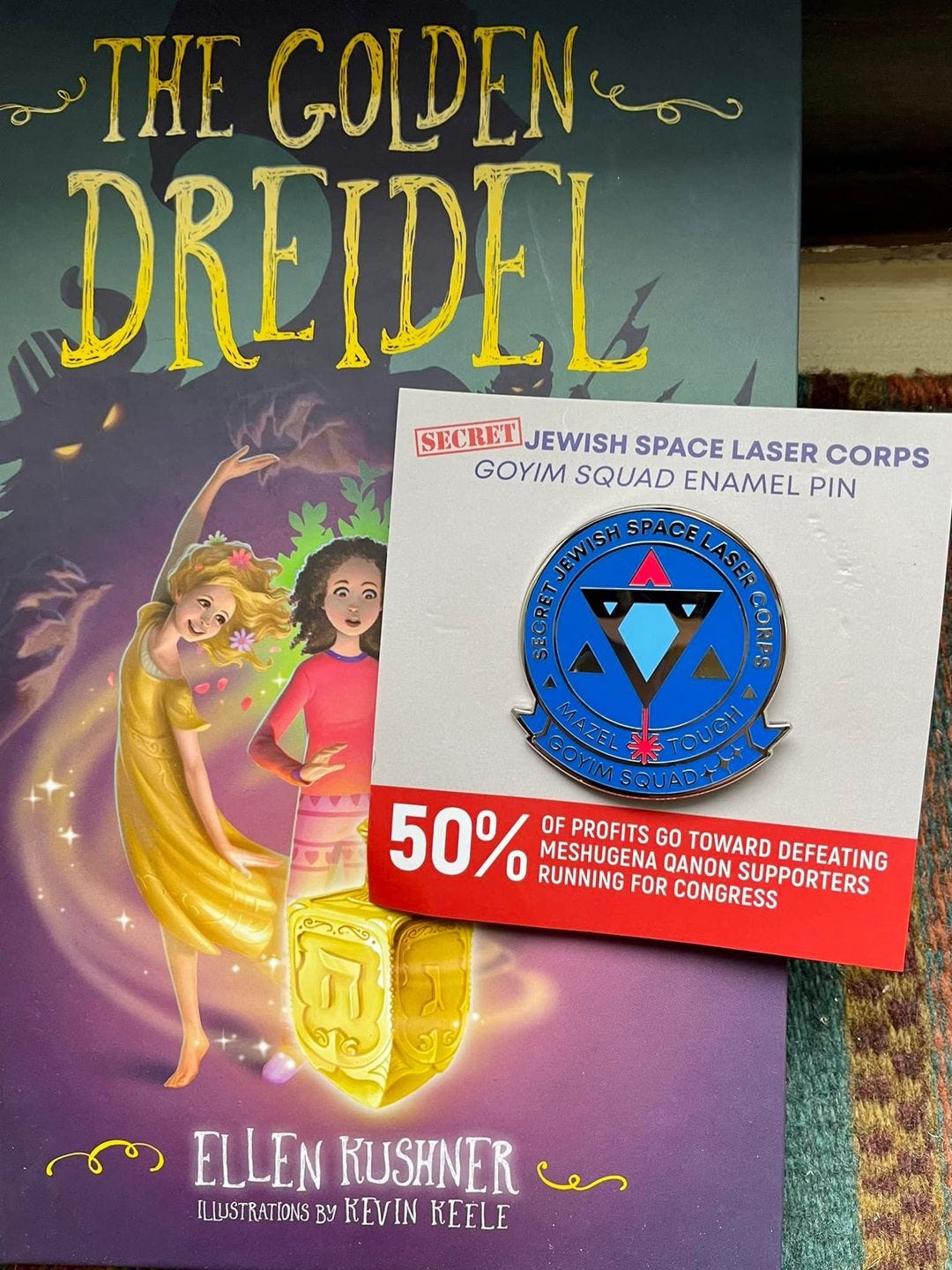 May be an image of text that says 'THE GOLDENE DREIDEL SECRET JEWISH SPACE LASER CORPS GOYIM SQUAD ENAMEL PIN EW LASEF GANE GOYIM 50% OF PROFITS MESHUGENA GO TOWARD SUPPORTERS DEFEATING RUNNING FOR CONGRESS QANON ELLEN KUSHNER e ILLUSTRATIONS By KEVIN KEELE'
