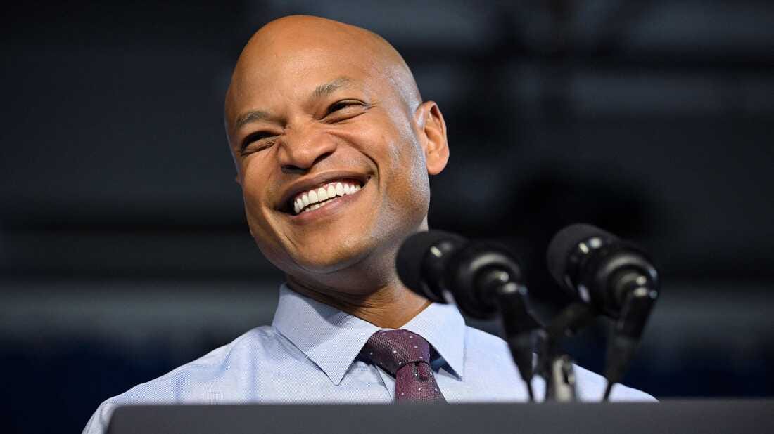 Photo of Wes Moore smiling in front of microphones at a podium.