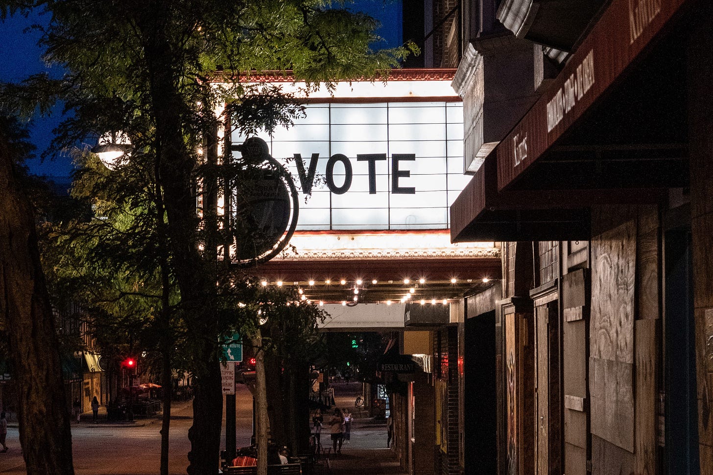 Movie theatre marquee with the word “VOTE” and a tree, at night