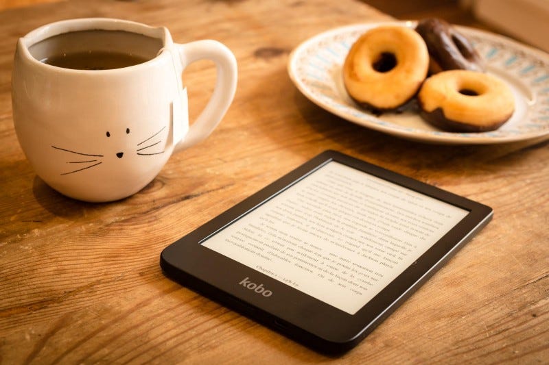 Kobo ereader, donuts, and coffee in a cat mug on table