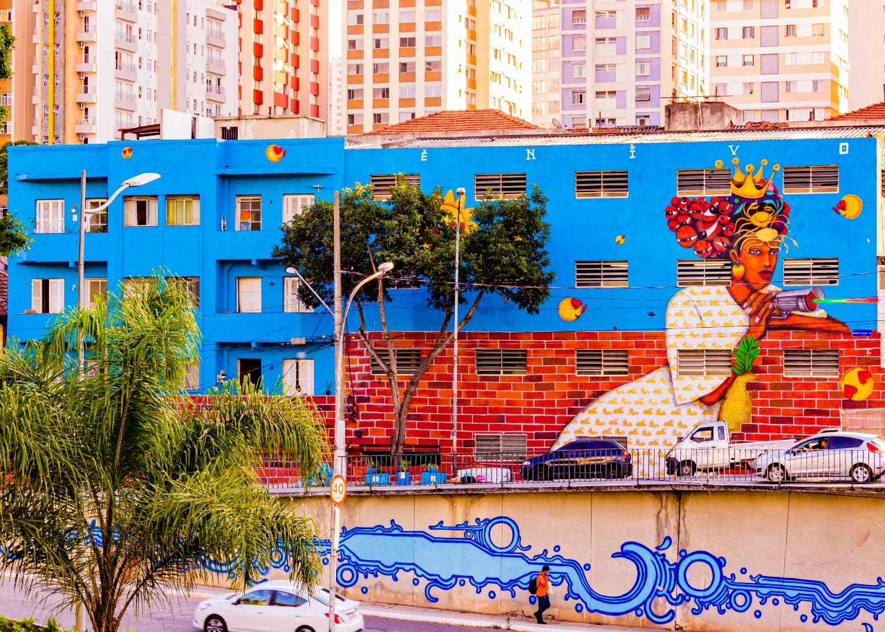 Grafite colorido em um prédio azul com mostra mulher com sementes de guaraná na cabeça. Artista: Enivo.