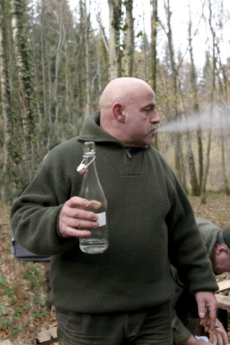 The tough looking bald guy drinking booze from a glass bottle.