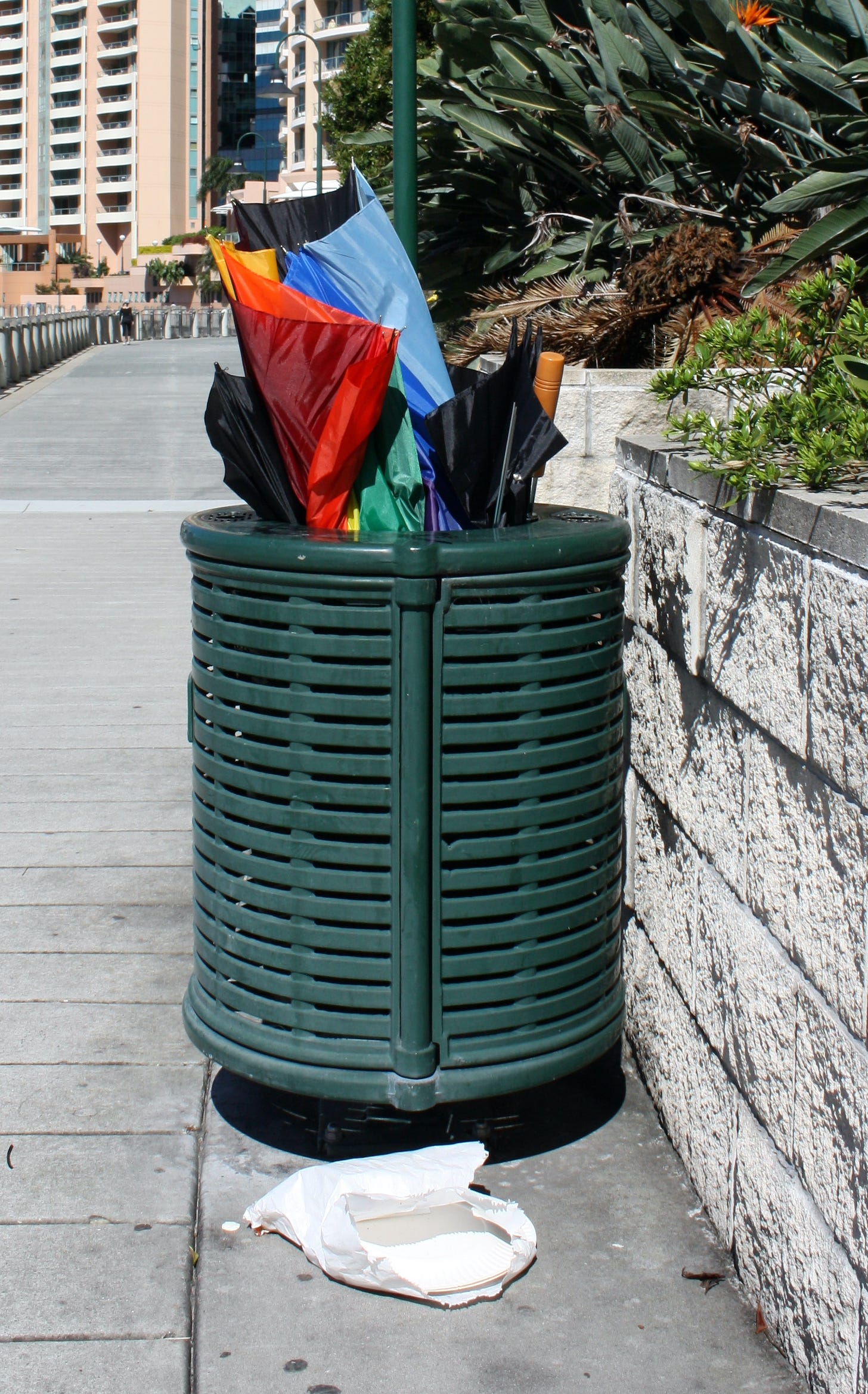 A trash can filled with umbrellas on a sunny day after a storm