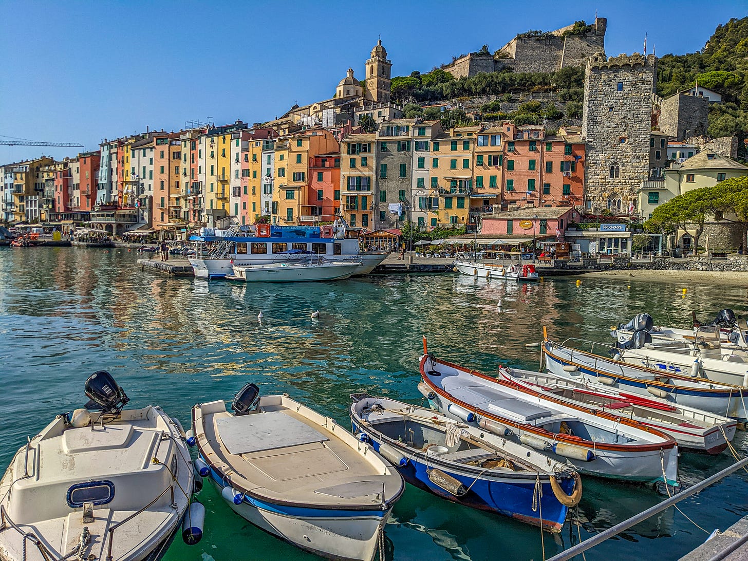 Portovenere's colorful waterfront with empty boats docked in the foreground, the colorful buildings of town on the other side of the water. 