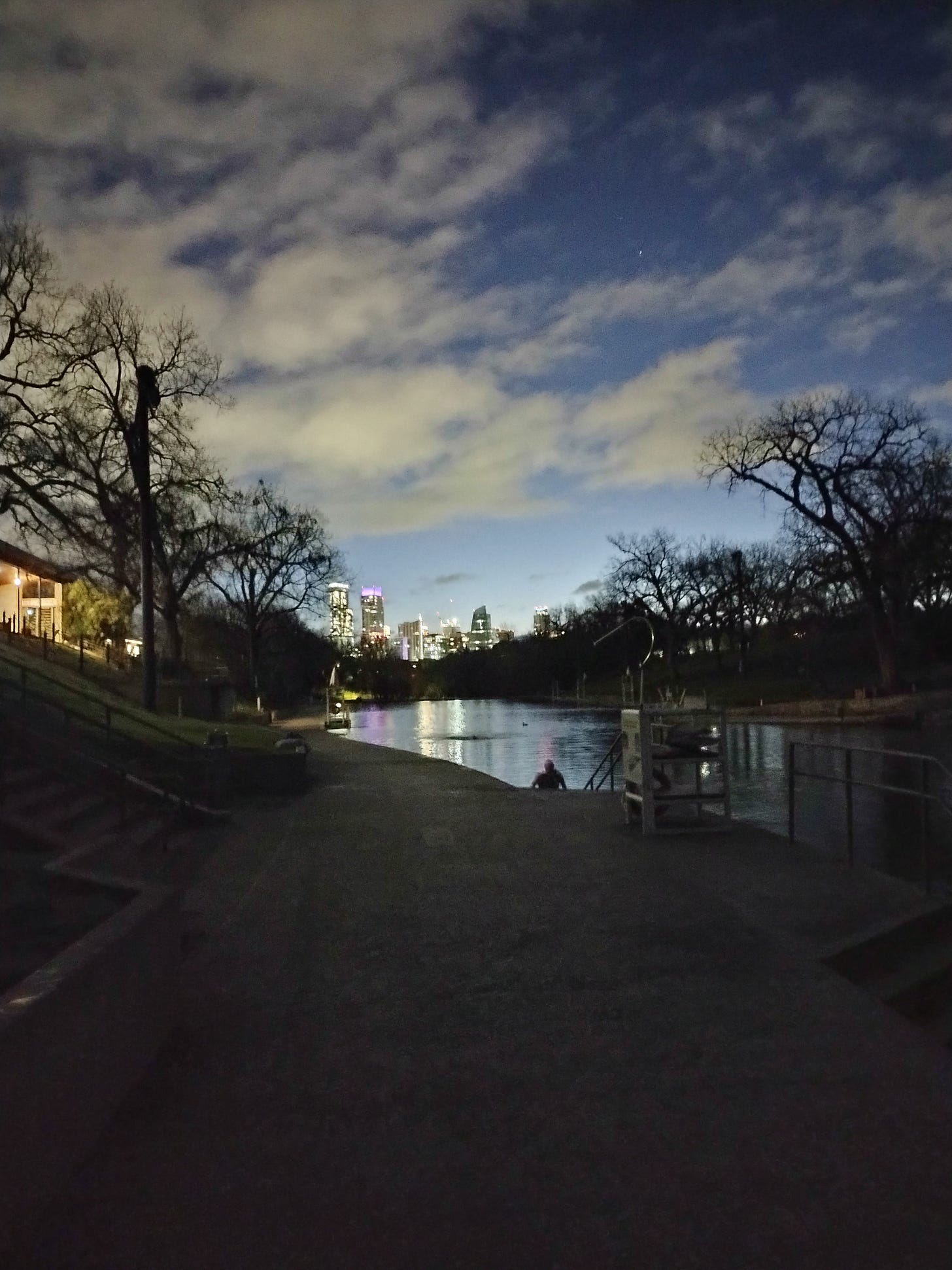 Barton Springs pool at dawn, skyline at the far end, water flanked by bare trees