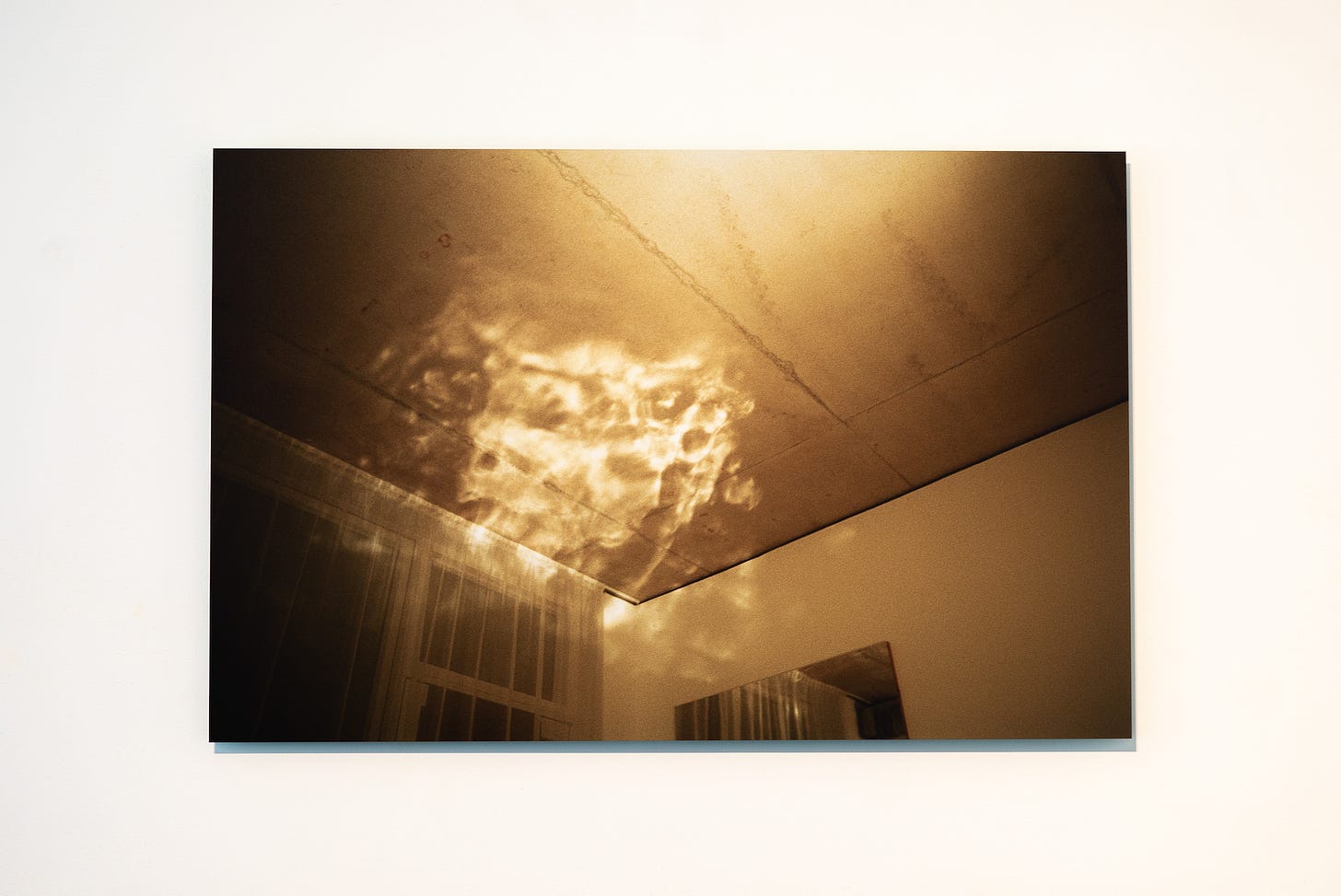 A horizontal rectangular image of light filtered through some sort of prism almost, diffused and amorphous, it dances upon the corner of a ceiling