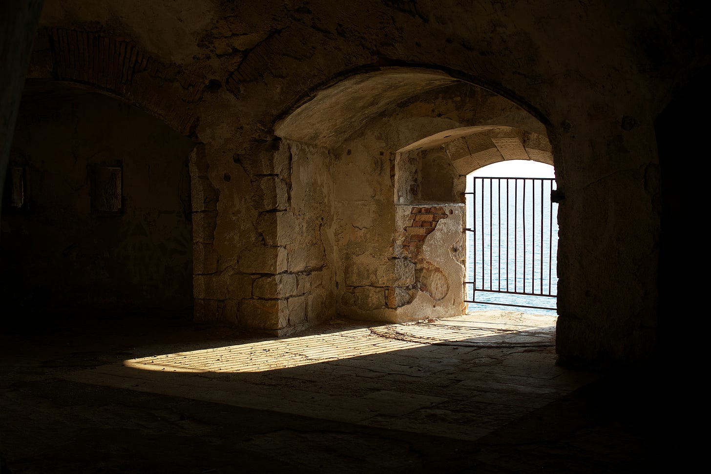 A gate in front of a window to the ocean, seen from inside a stone building