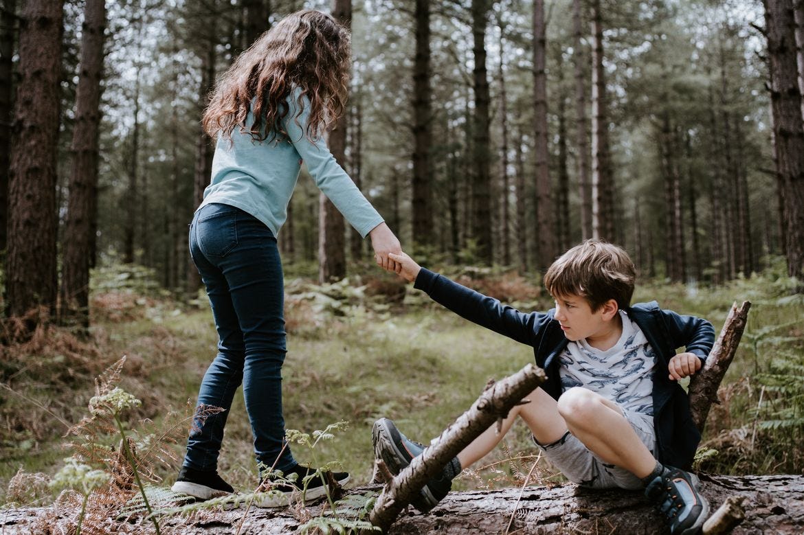 Child helping another child get up in a wooded area