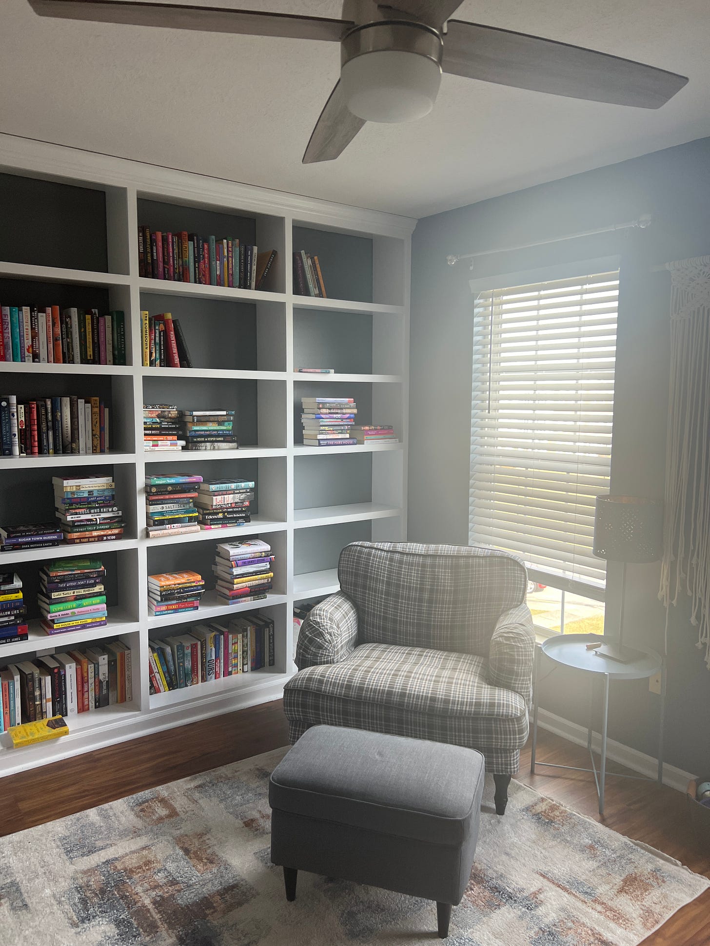 A plaid armchair in front of white built-in bookshelves with tons of books on them.