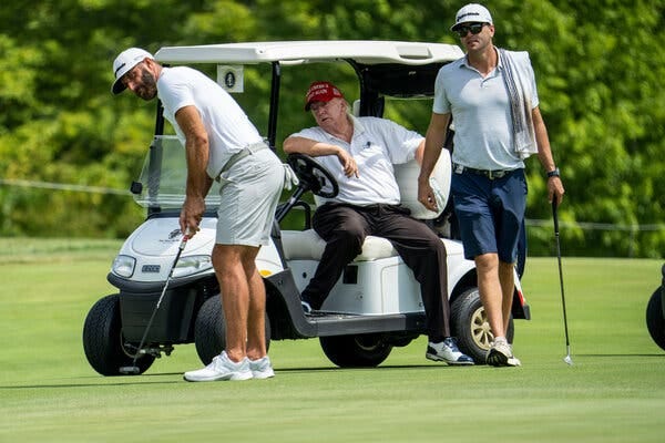 Former President Donald Trump, seated in a golf cart, watched golfer Dustin Johnson putt as another golfer watches.