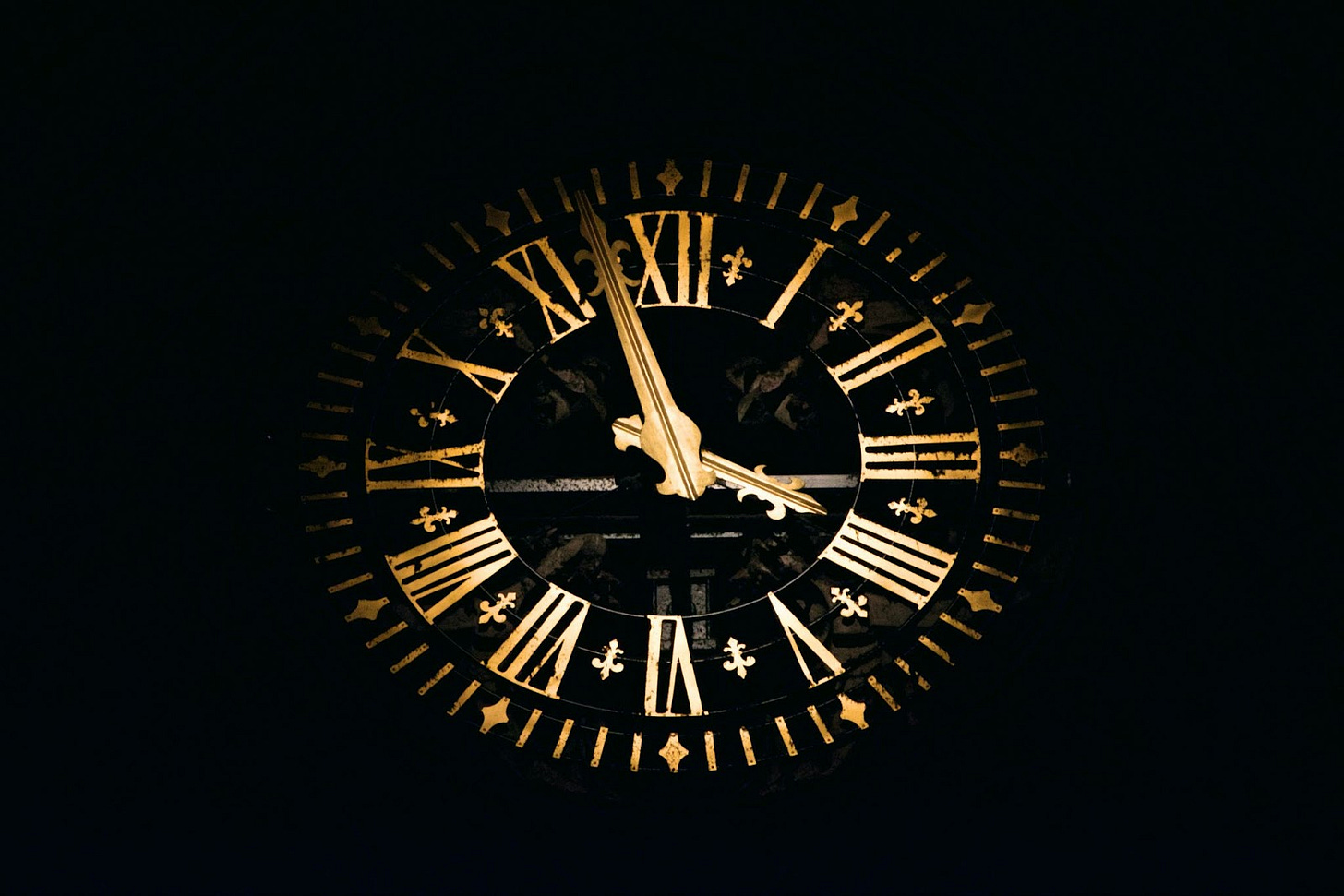 A glowing, golden clock showing the hours in roman numerals set against a black background. A glowing, golden clock showing the hours in roman numerals set against a black background.