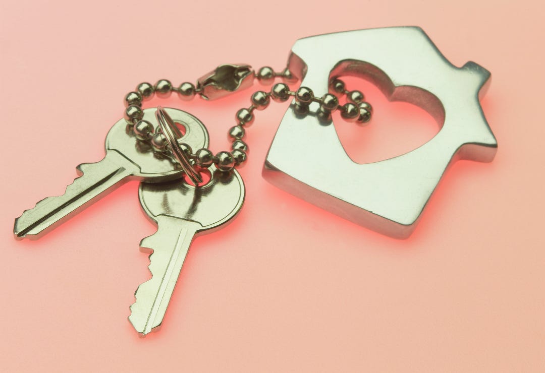 gold keychain holding a charm in the shape of a house with a heart in the middle attached to two keys against a peach background