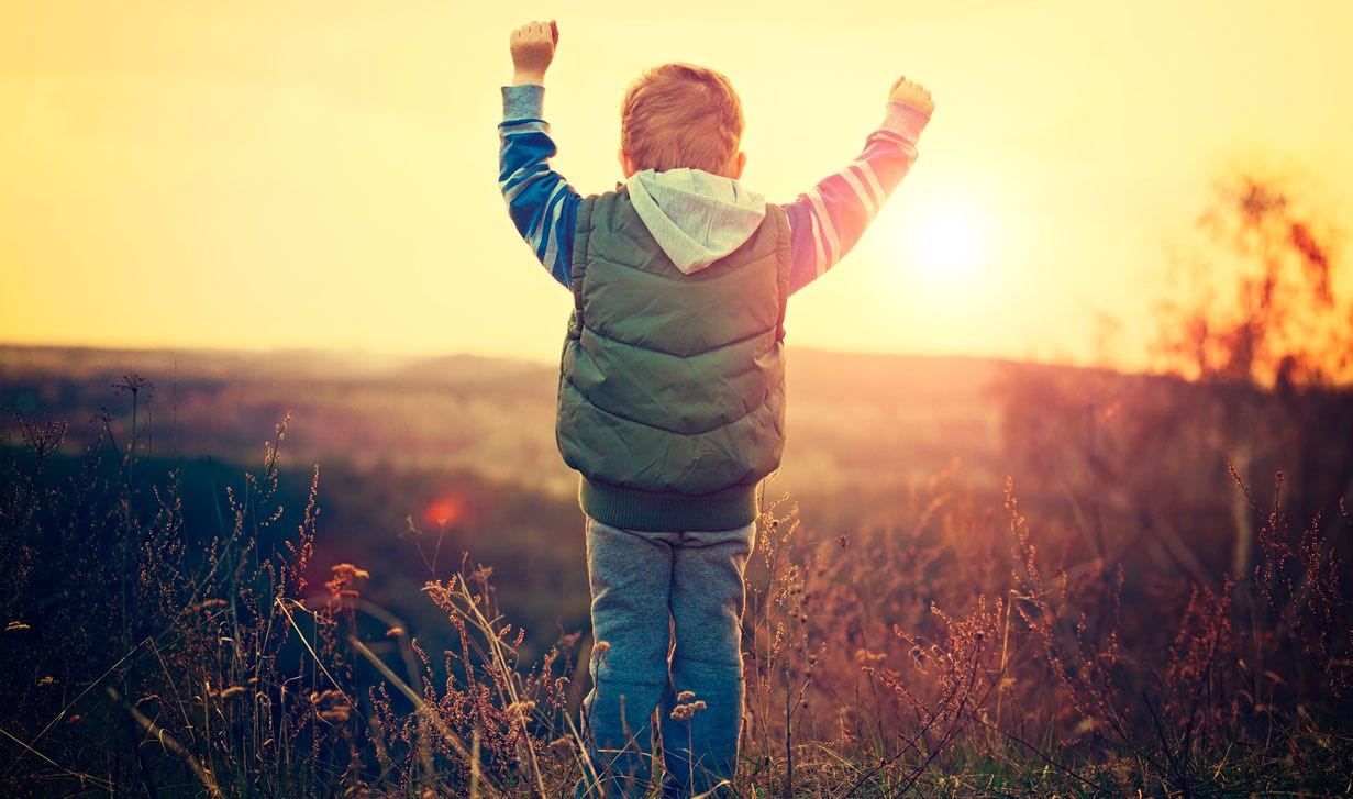 Little boy, about five years old, back to the camera with his arms raised to the sunrise.