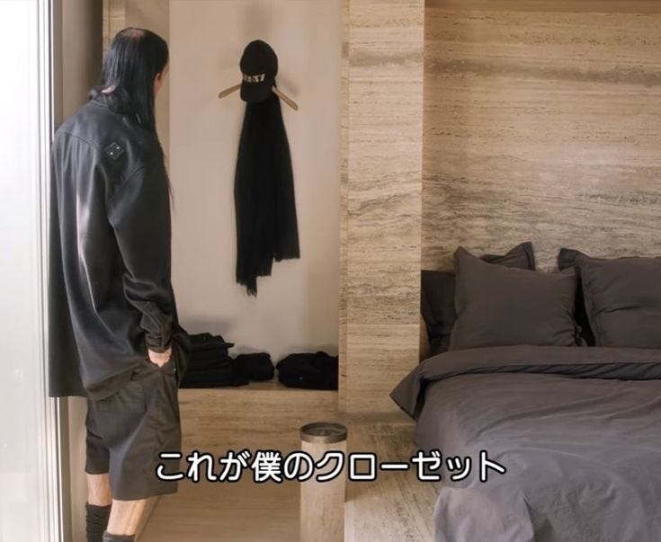This may contain: a man standing in front of a bed with clothes hanging on the wall