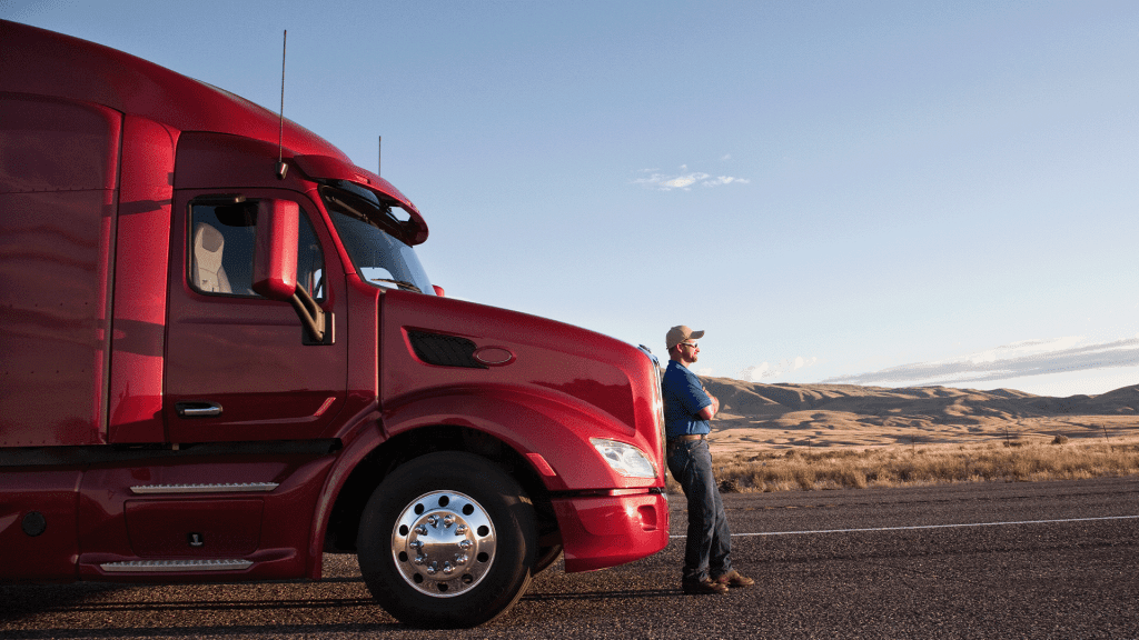 Truck driver leaning on the grill of his commercial truck