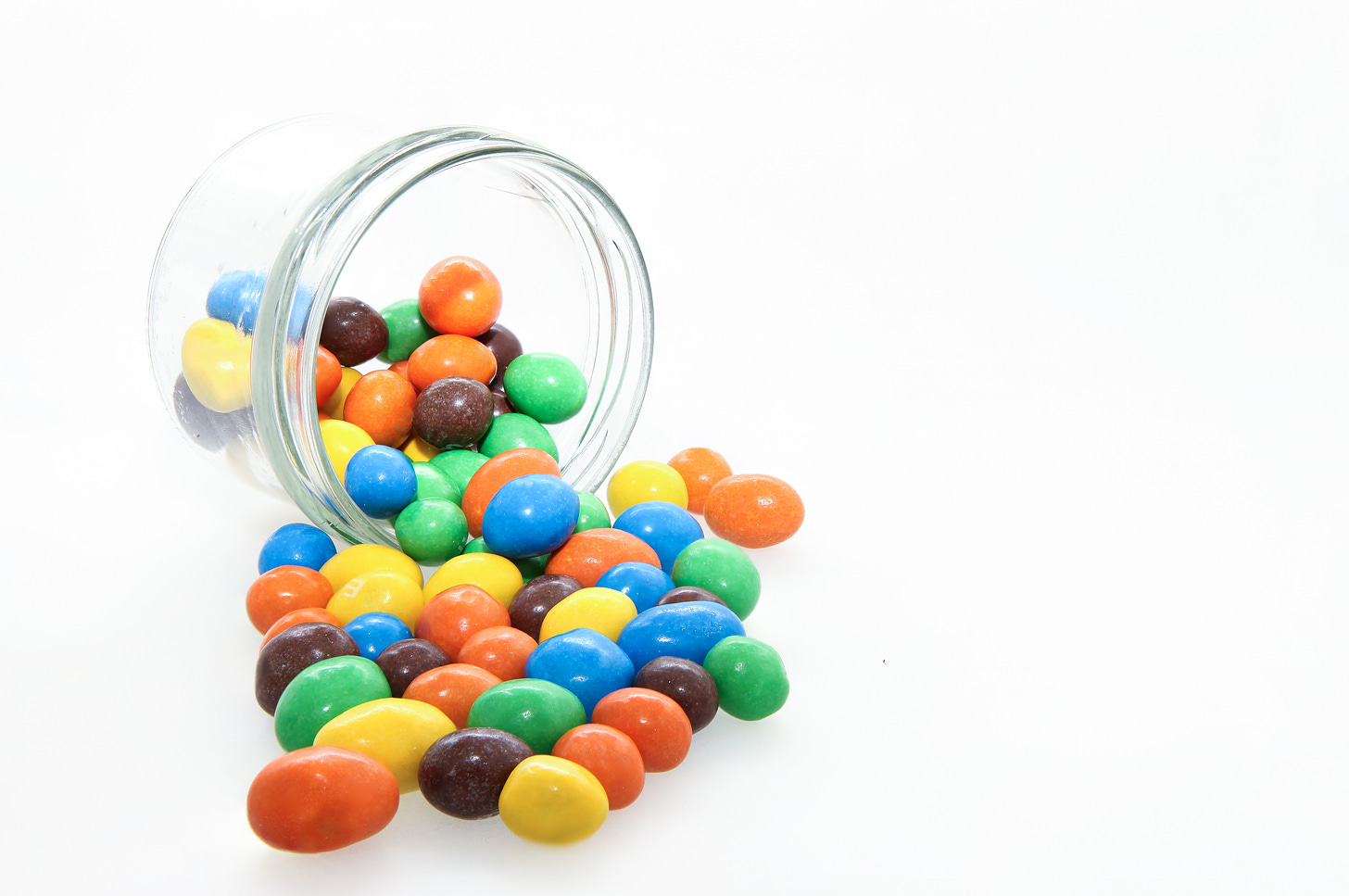 Glass jar on its side with candy-coated chocolate spilling out