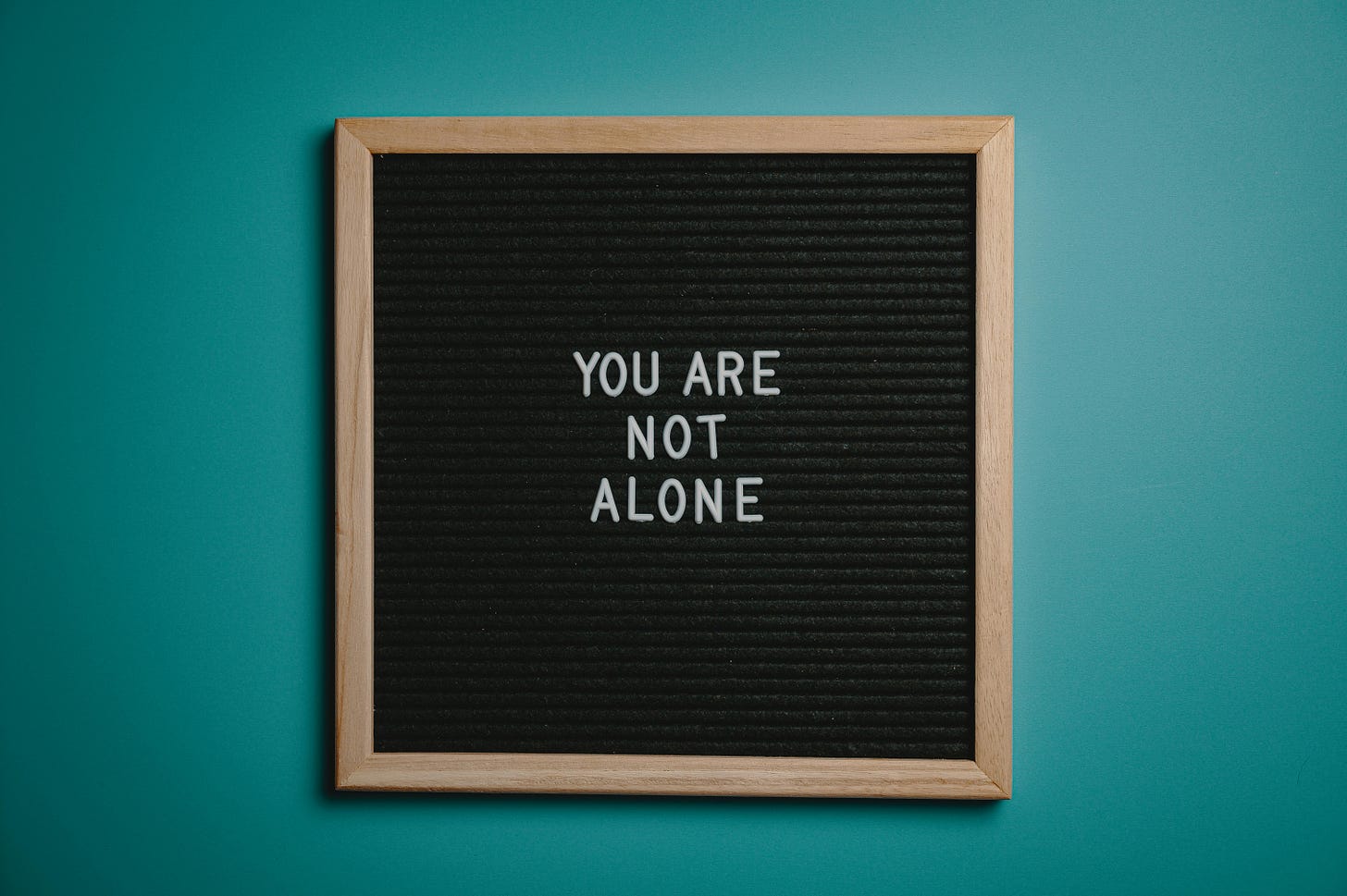 The words “You are not alone” appears on a board on a teal wall.