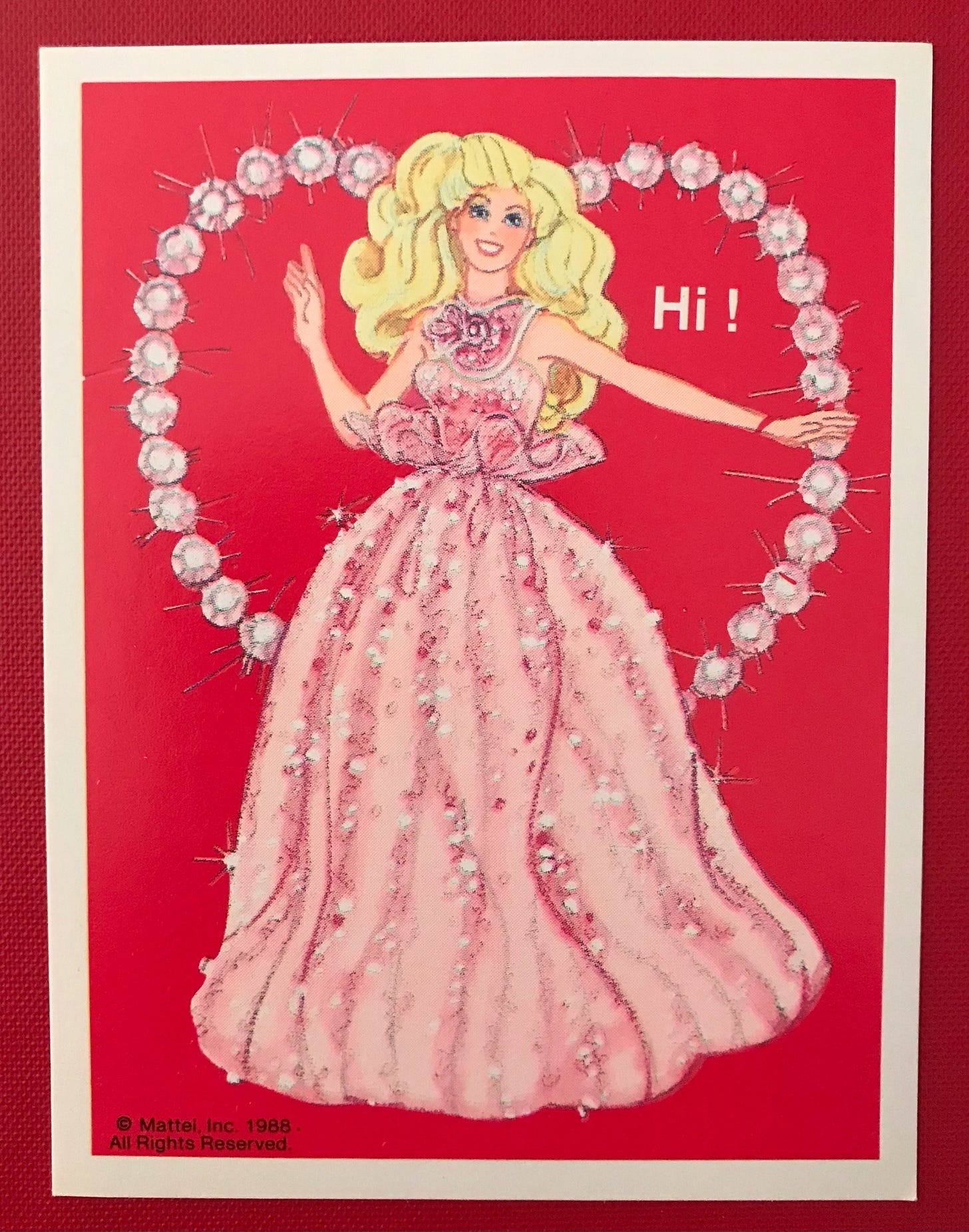 A red and pink Barbie valentine featuring Barbie in an elaborate pink sparkly dress in front of a heart-shaped ring of gems. Text: Hi!