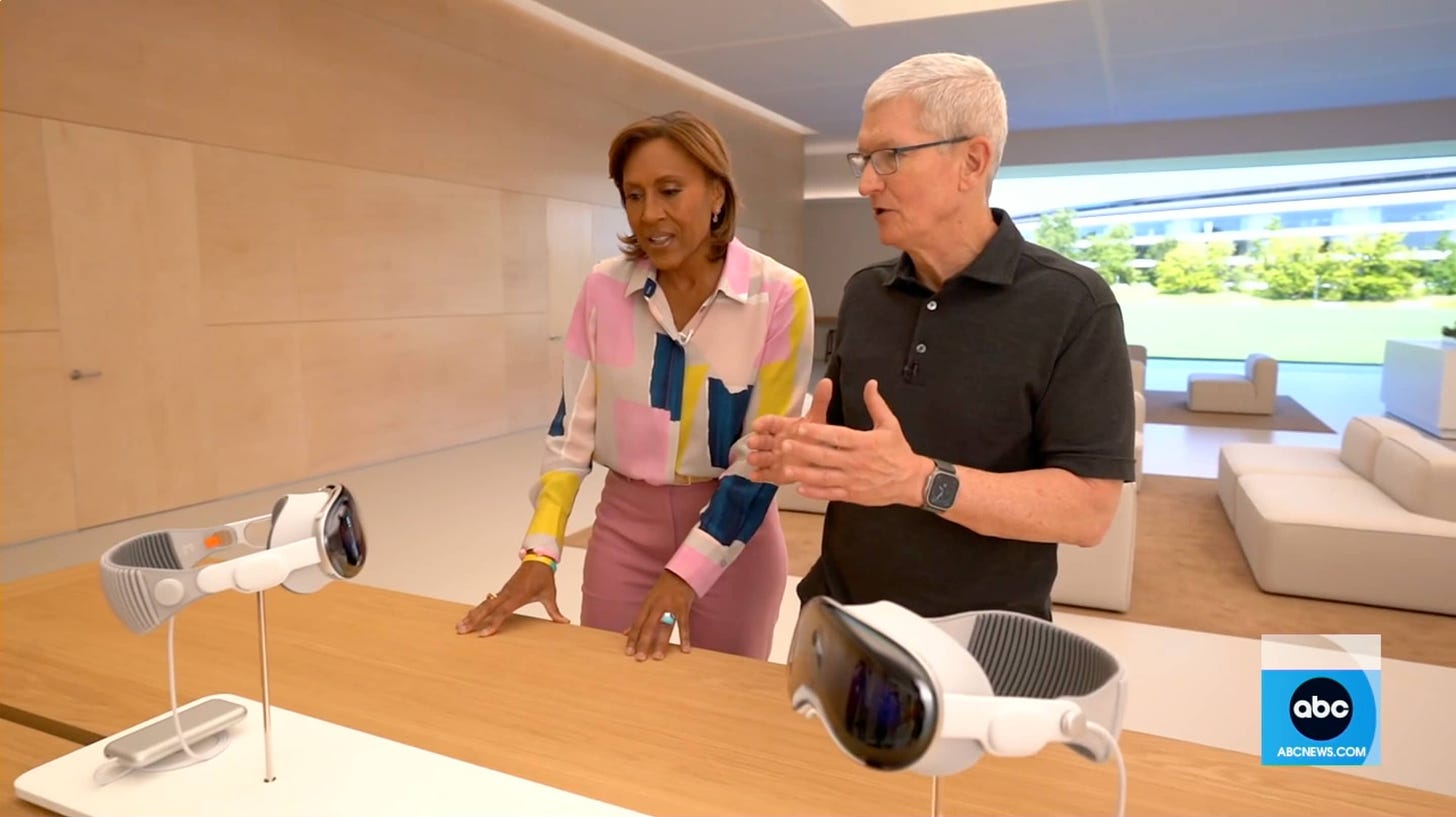 Robin Roberts and Tim Cook look at a riser holding two Apple Vision Pro headsets.