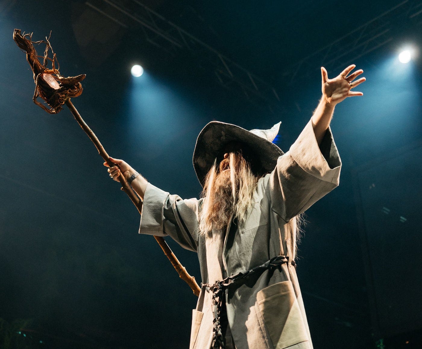 An actor in a wizard's cloak and hat stands with his arm's aloft.