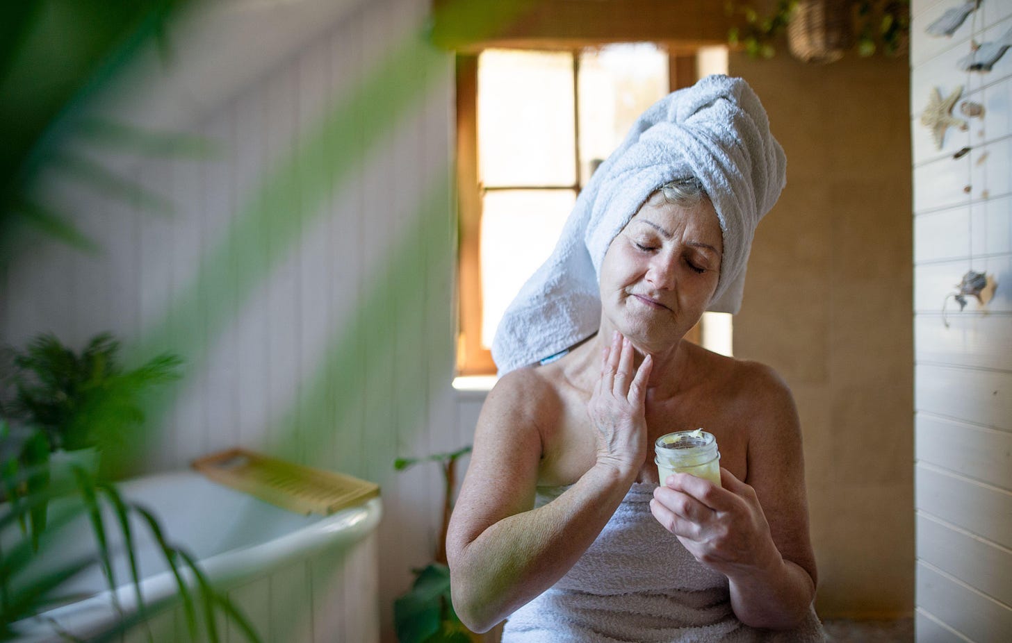 Happy senior woman wrapped in a towel applying homemade body moisturiser.