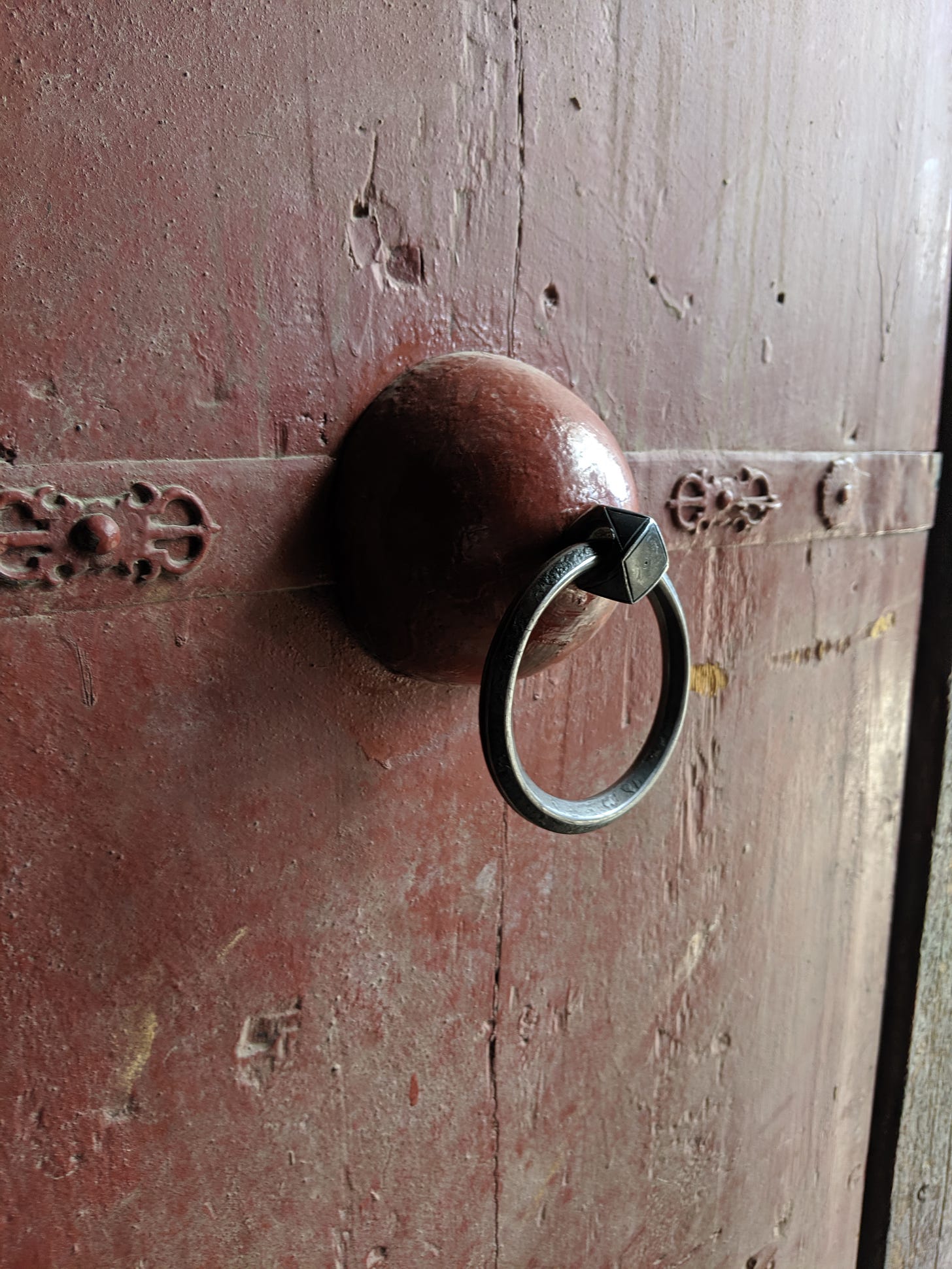 A reddish wooden door with a large brass ring knocker