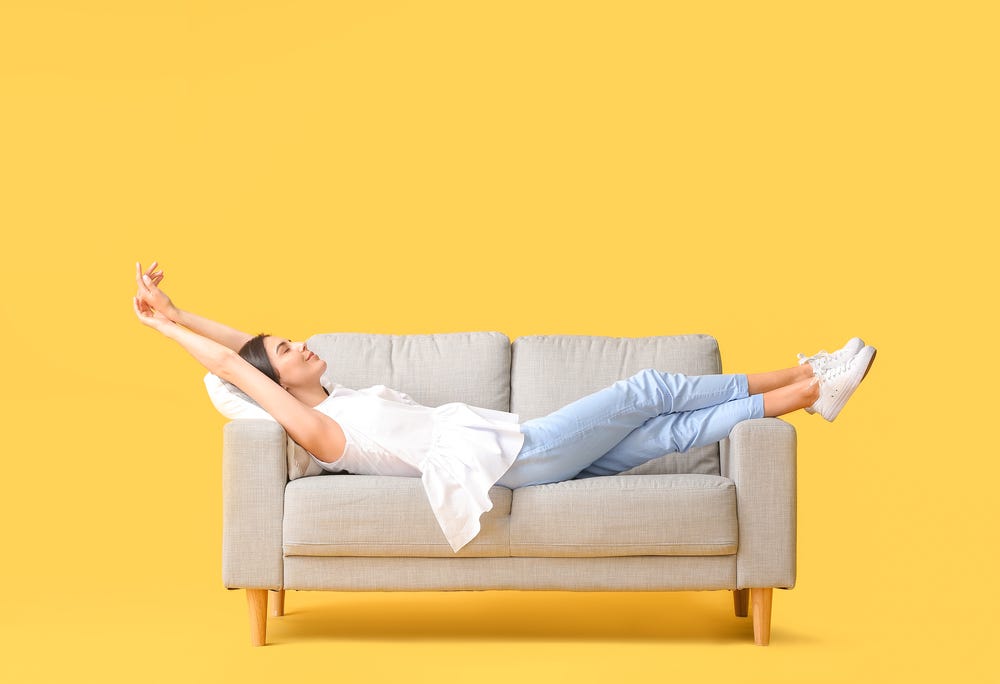 A woman stretched out on a sofa, alone, looking really happy about it.