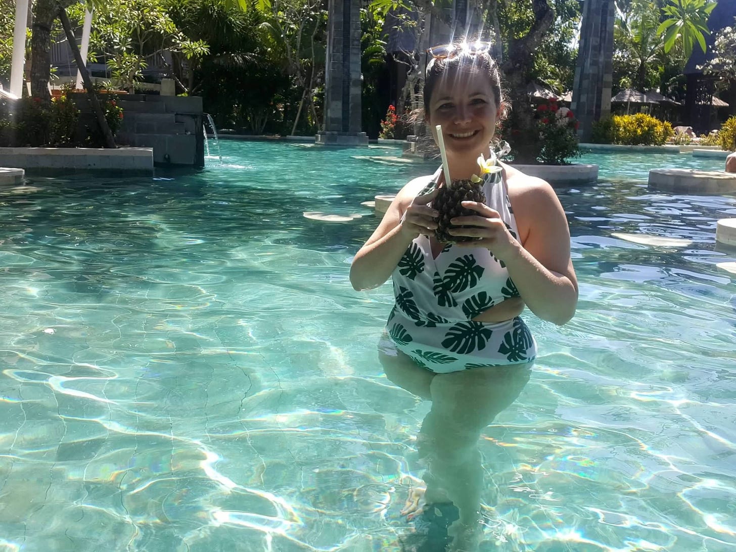 The author stands in a tropical pool holding a cocktail inside a pineapple