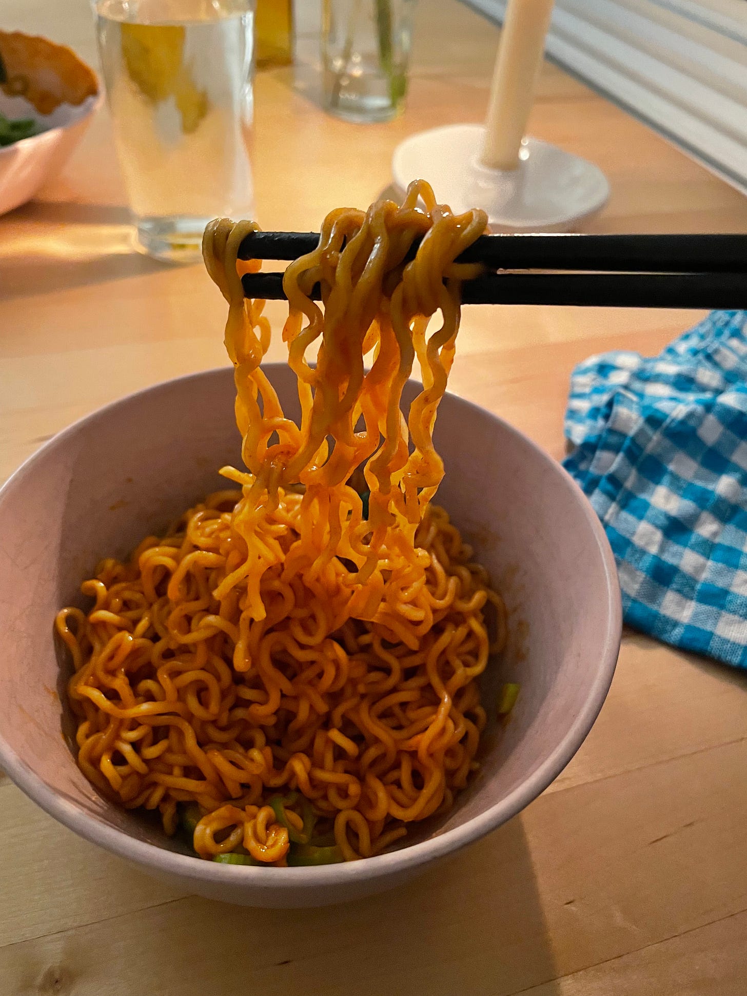 Chopsticks lifting gochujang noodles from a pink bowl.