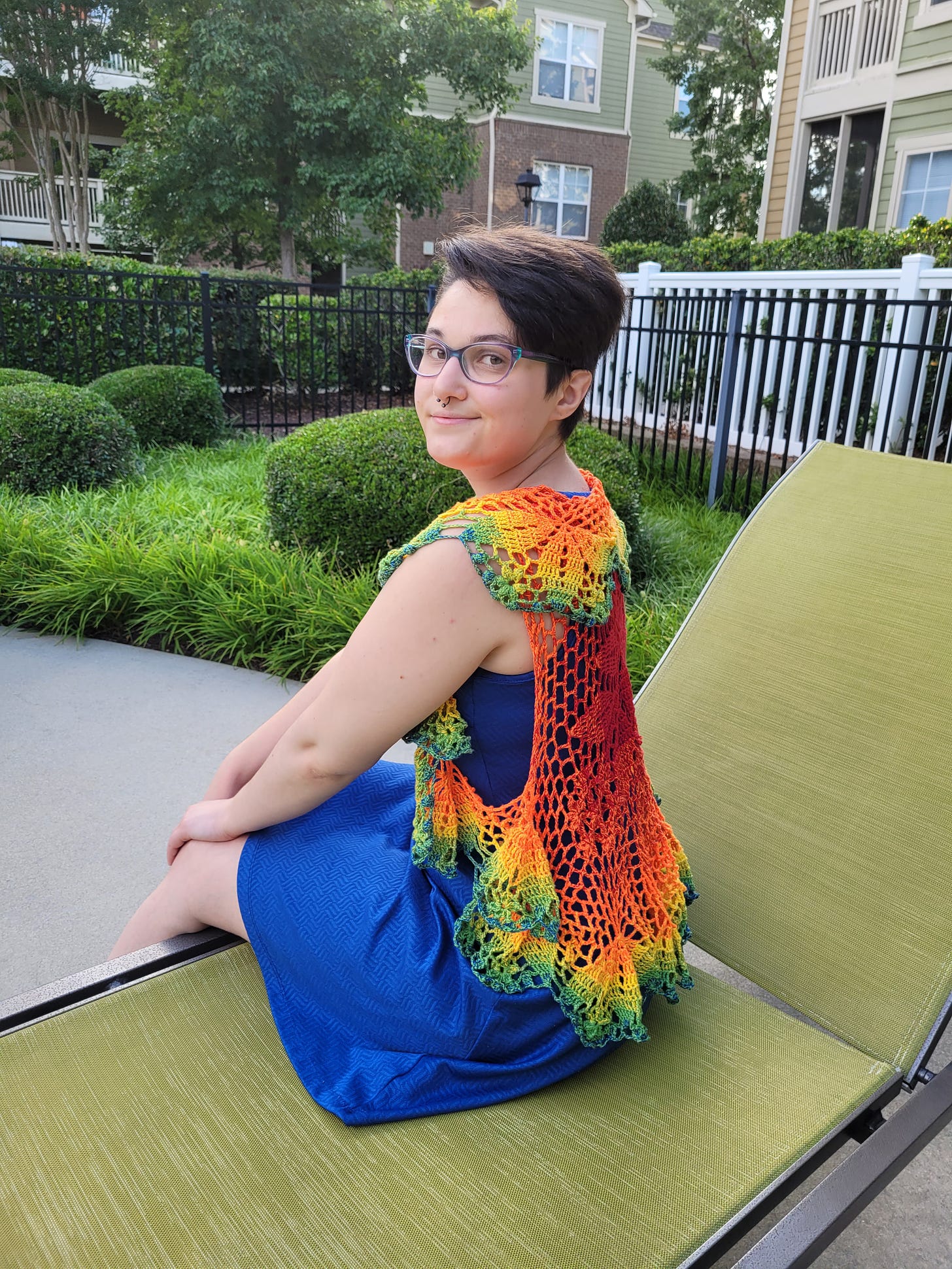 V "Kitty" wearing a handmade rainbow knit shawl sitting on a outdoor lounge chair.
