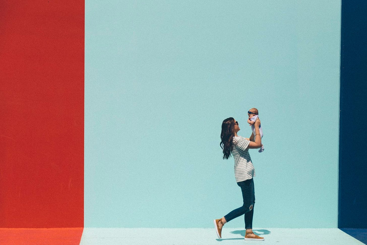 Profile of woman holding up baby against a blue background.