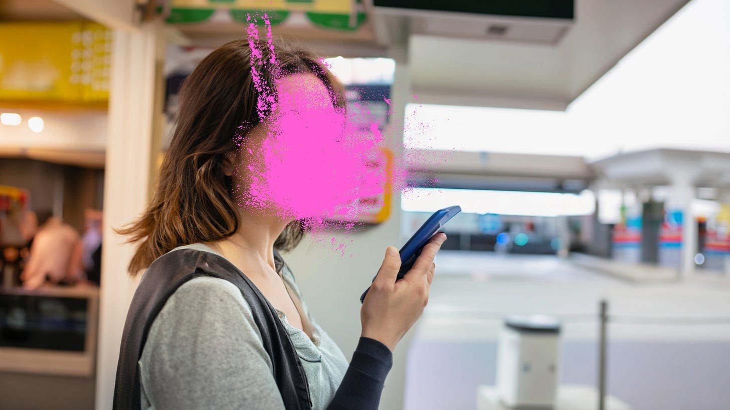 A young, brown-haired woman, holding her phone to her face as she waits for a pretzel at a service station beside a highway. Her face is covered to protect her anonymity.