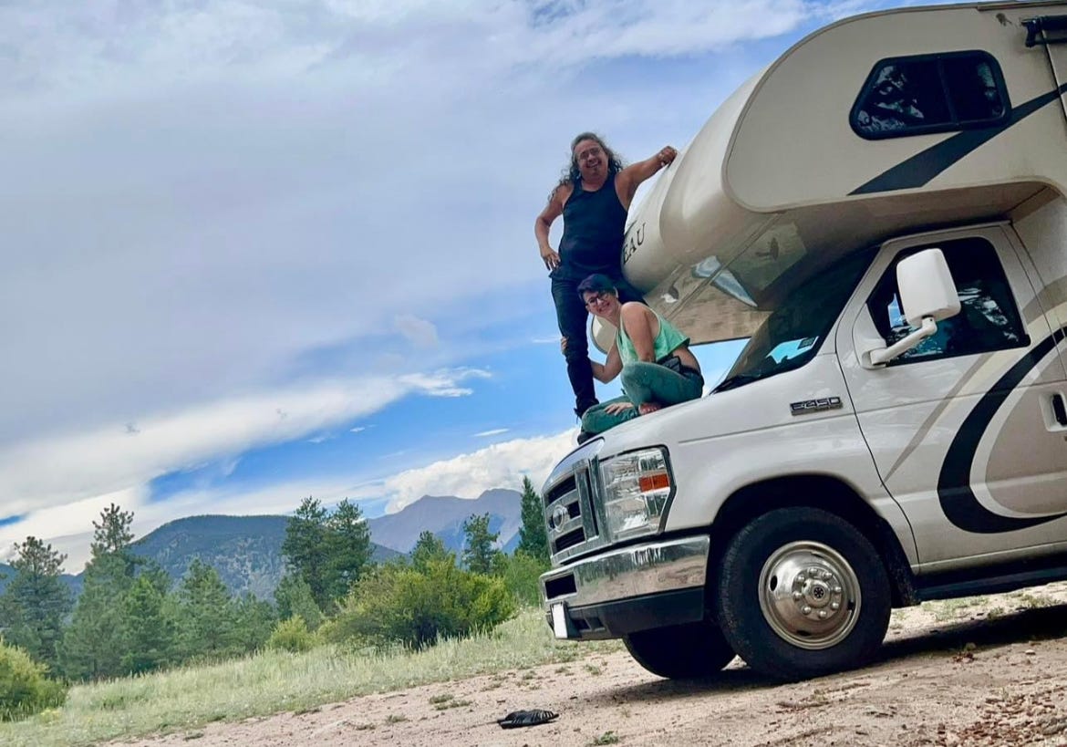 Lyric and David sitting on the hood of their RV, with the Colorado mountains in the background. 