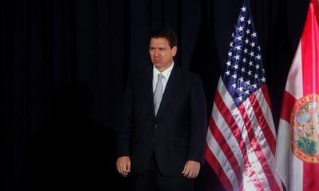 Ron DeSantis looking glum next to an American flag