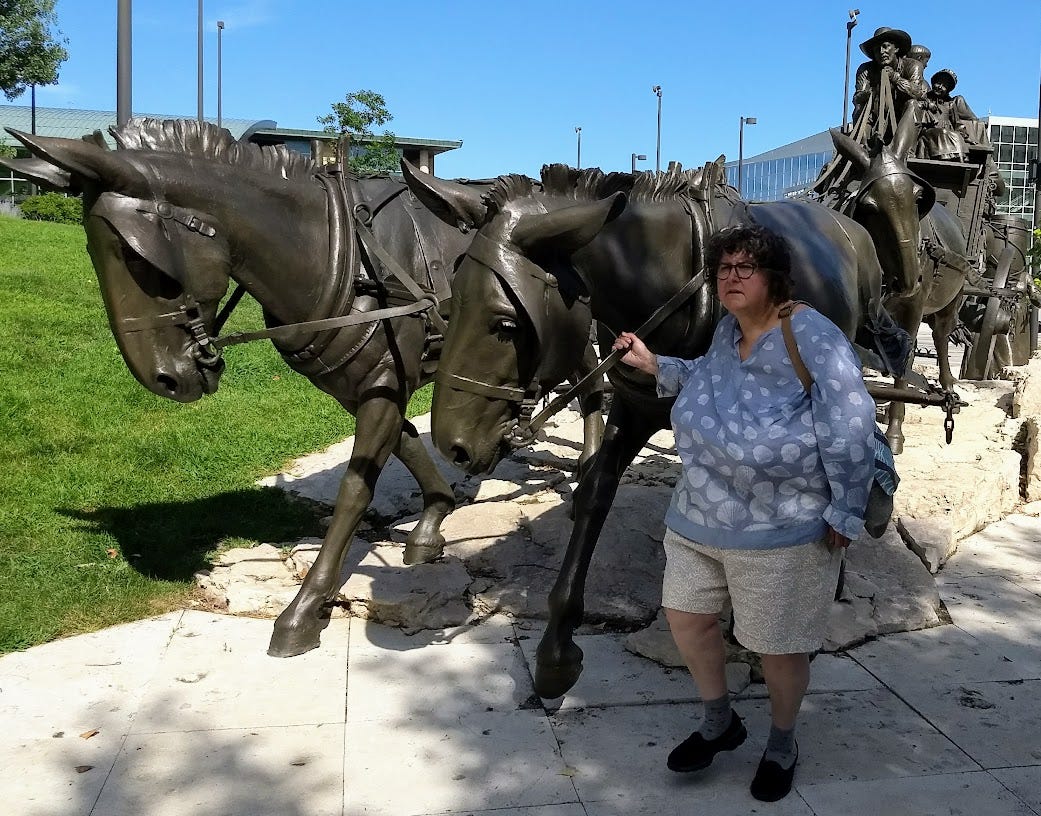 Woman leading mule statues pulling wagon statue with tall buildings in background