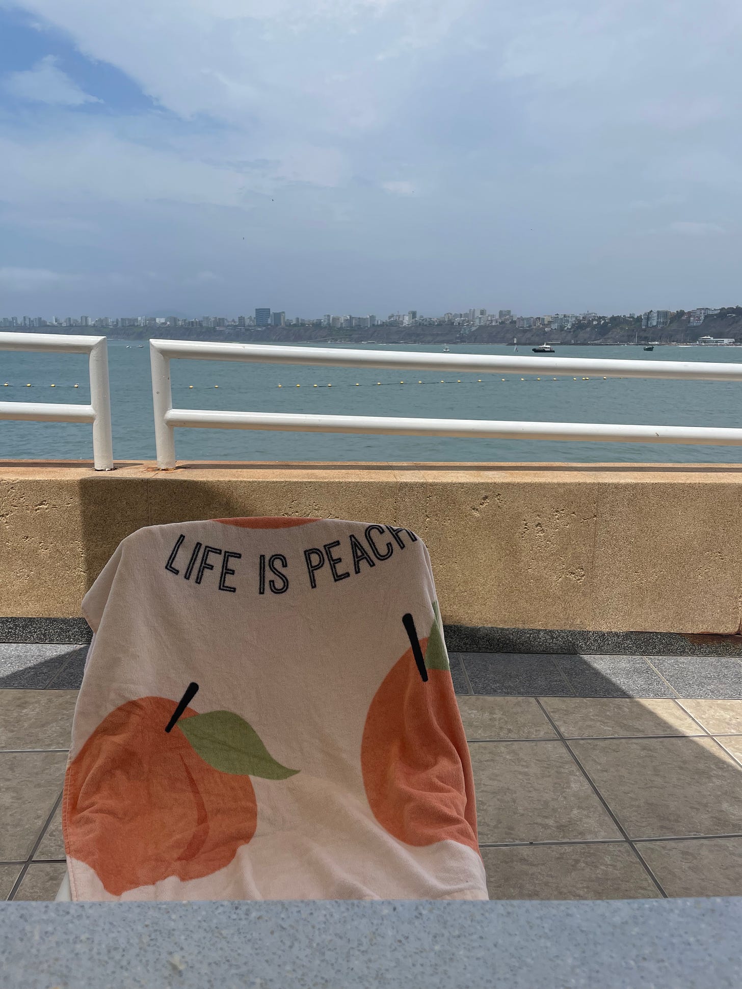 A towel with the words Life Is Peach is draped over a beach chair overlooking the ocean