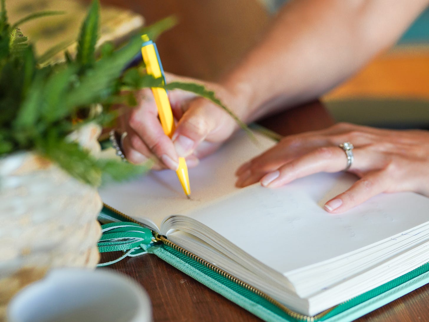 picture of a hand with a yellow pen writing in a journal