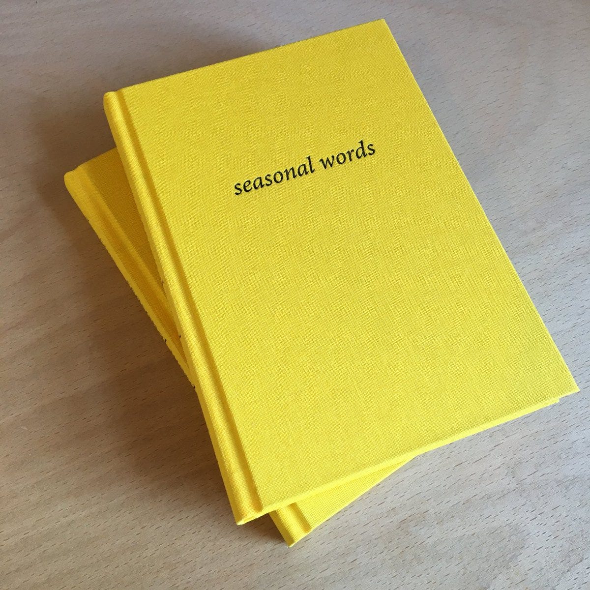 A small stack of books with bright yellow clothbound covers with "seasonal words" embossed in black.